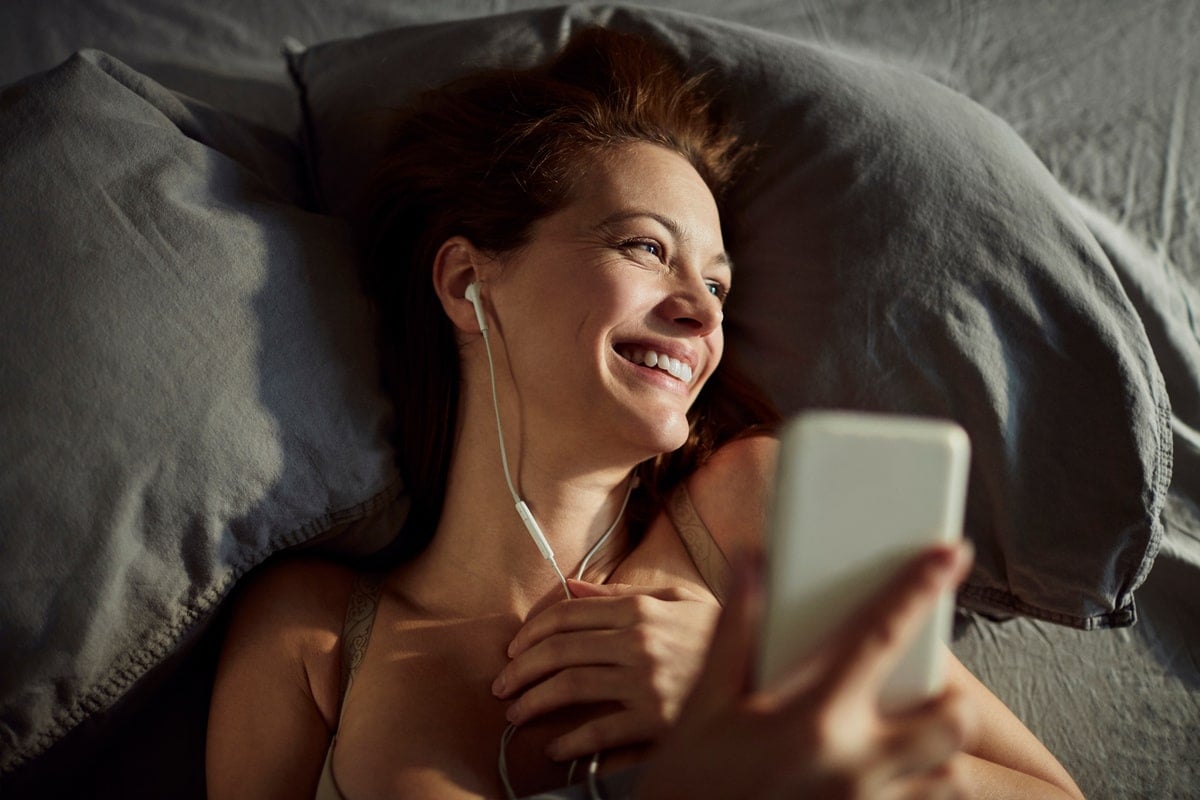 Vrouw die met haar telefoon in bed ligt - een van de redenen voor het slecht slapen